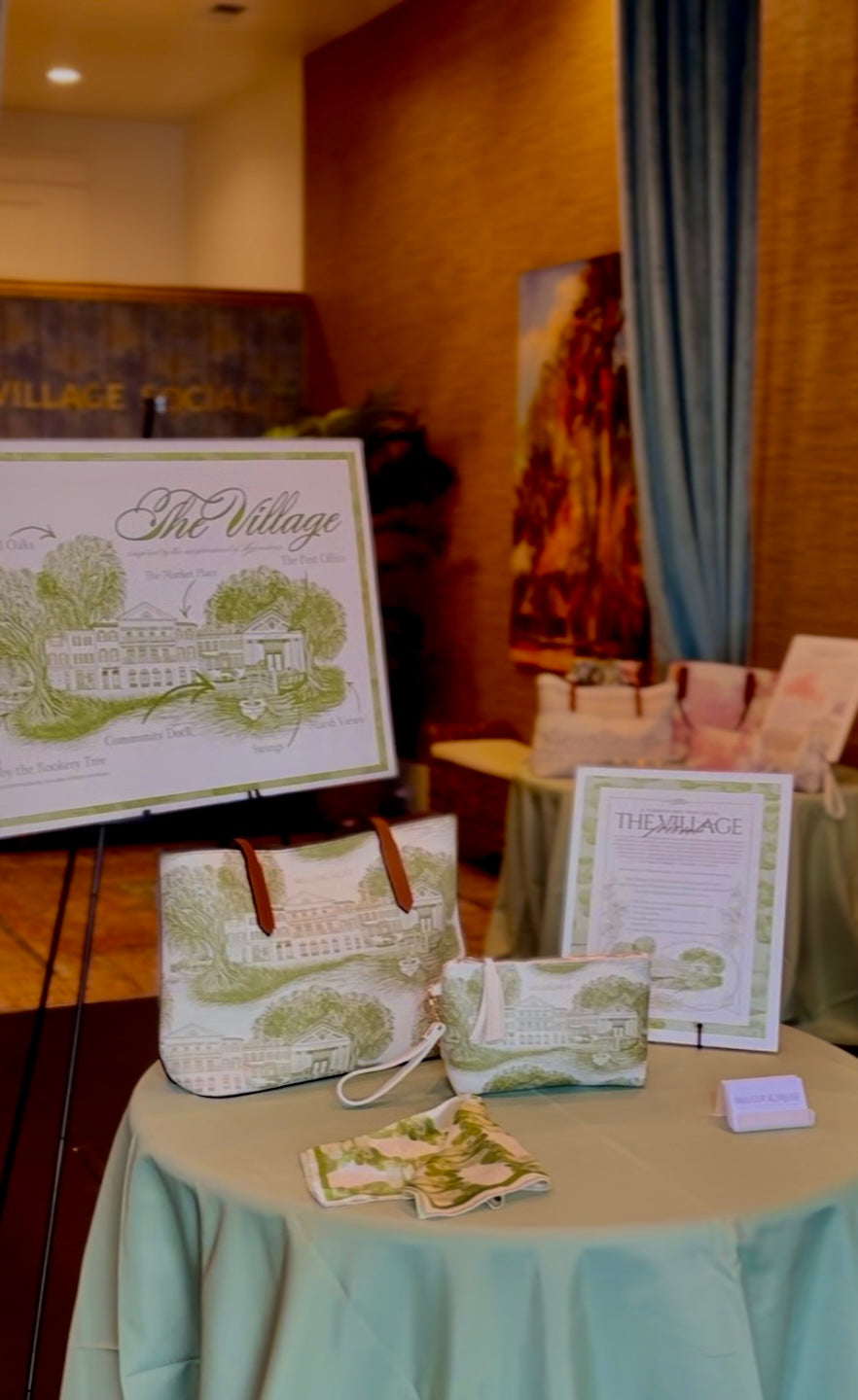 Table with branded totes, cometic cases and silk scarves and promotional materials in a room setting. The materials feature a green and white toile style design inspired by the neighborhood of Habersham in Beaufort, SC.